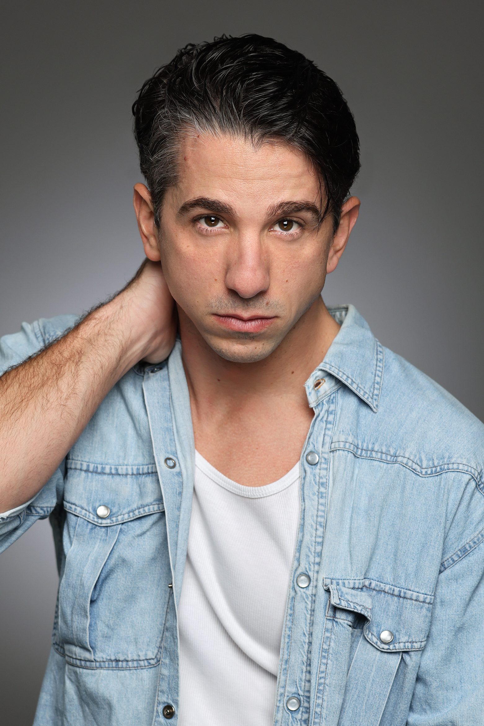 Javi Guerrero, actor, in a denim shirt with his hand on his neck